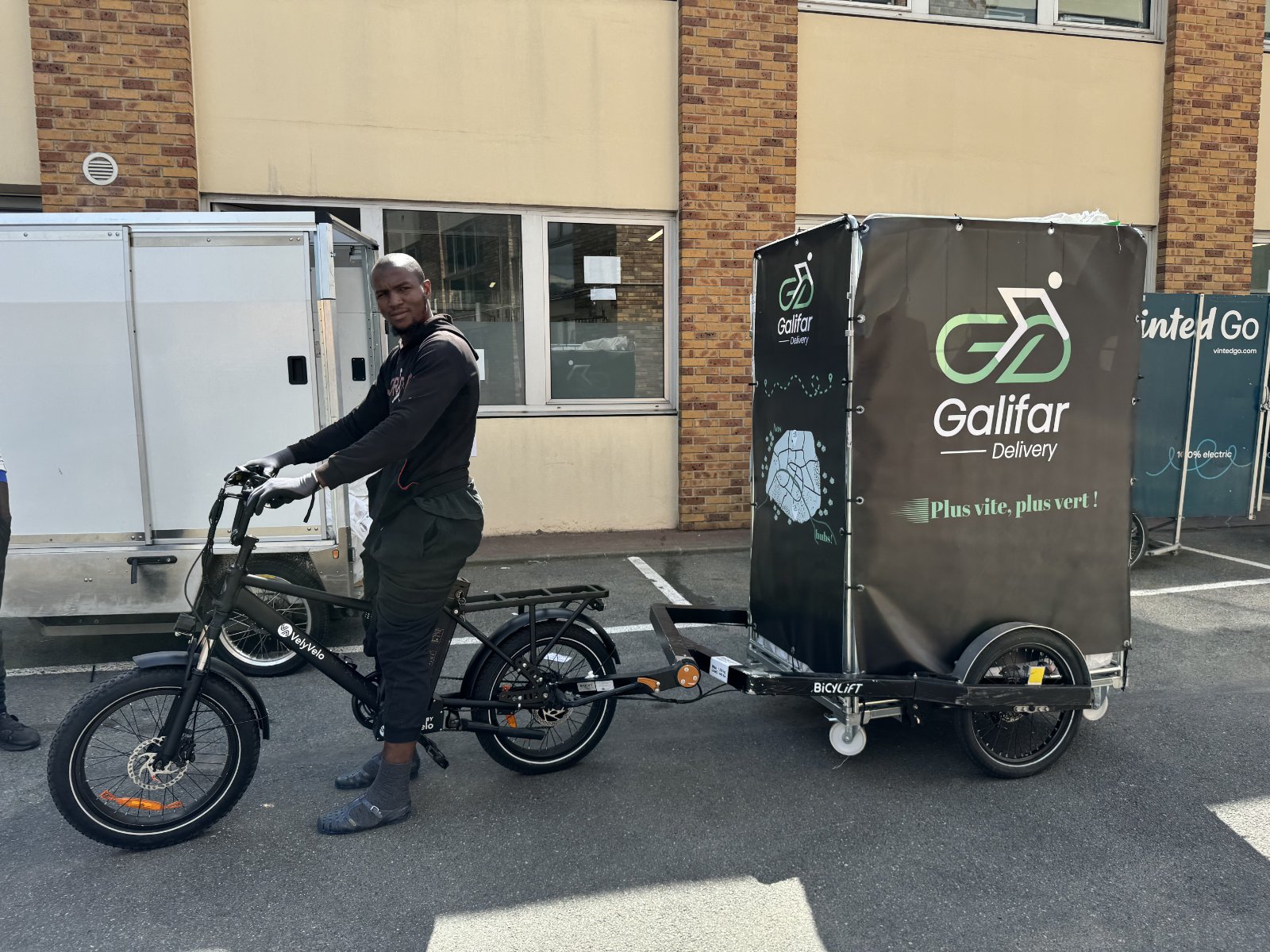 Coursier Galifar avec vélo cargo et remorque BiCYLift co-brandée Galifar Delivery × Vinted Go, devant le hub nord parisien